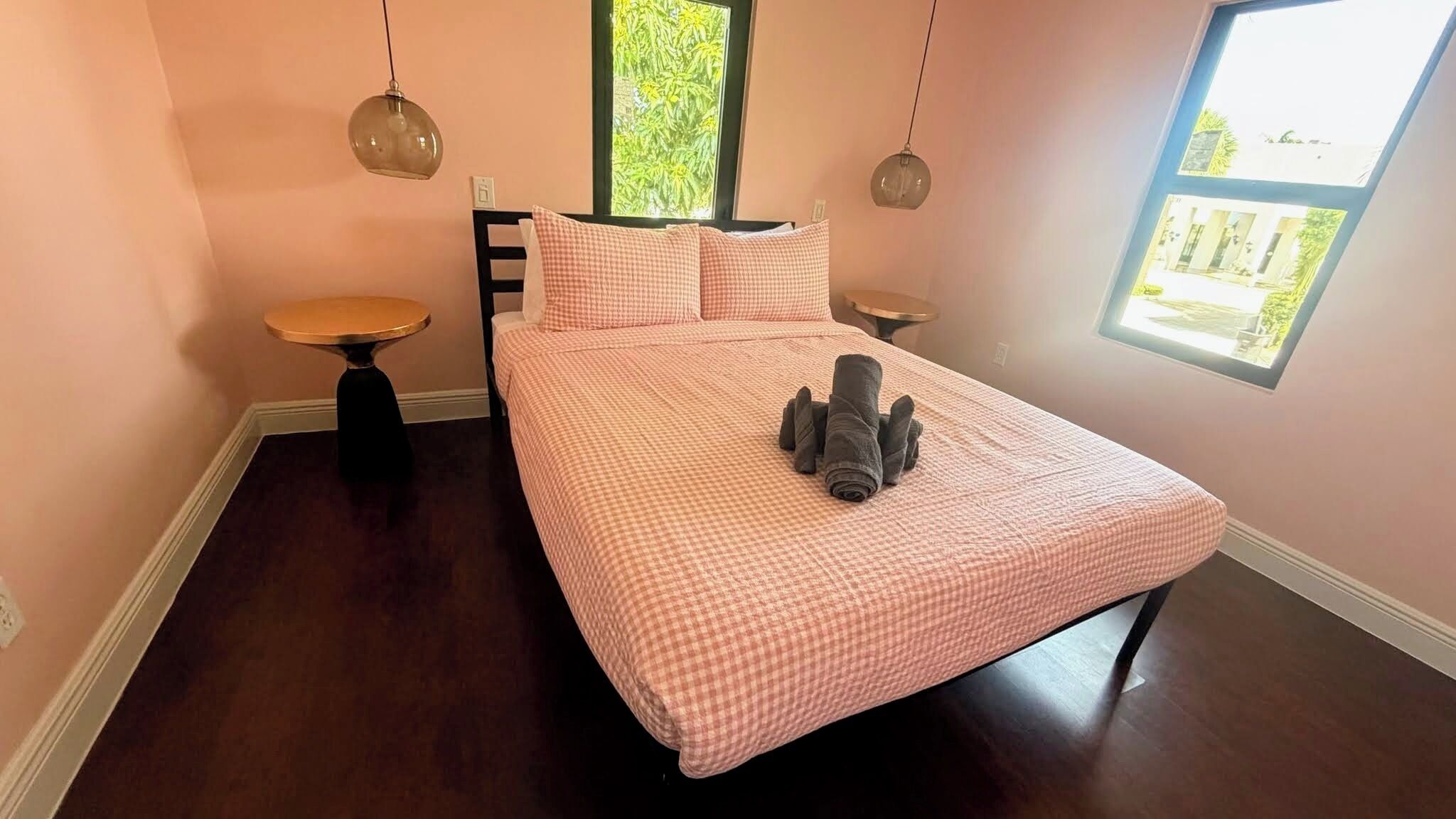 Een slaapkamer met een geruite sprei, twee nachtkastjes, een raam met uitzicht en een hangende lamp.