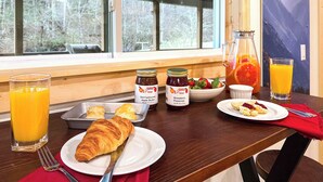 Une table de petit-déjeuner avec des croissants, un verre de jus d’orange, un pot de compote de pommes, une carafe de jus d’orange et un bol de fraises.