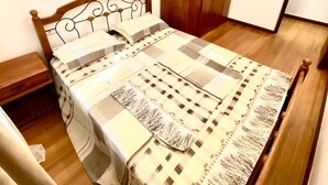 Un lit simple avec une tête de lit et un pied de lit en bois, une armoire en bois et une table de chevet dans une pièce aux murs unis et au plancher en bois.