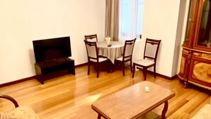 Un salon avec un plancher en bois, une table à manger avec des chaises, un téléviseur et un lustre.