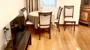 Une pièce avec un plancher en bois, une table ronde entourée de quatre chaises, un canapé, un meuble et une fenêtre avec des rideaux.
