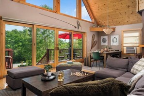 A spacious living area with a large sliding glass door leading to an outdoor deck, a cozy seating arrangement, and a dining area with a table and chairs.