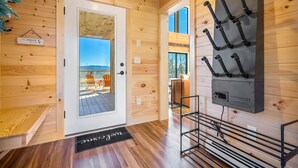 A wooden interior with a door leading to an outdoor area, a wall-mounted rack, and a bench.