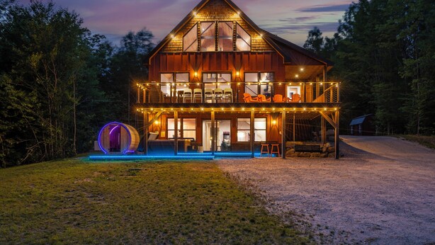 A large, two-story wooden cabin with a balcony, surrounded by trees.