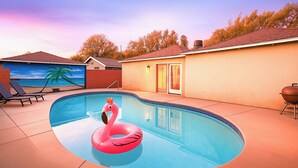 Une piscine avec un flotteur en forme de flamant rose, des chaises longues et un barbecue.