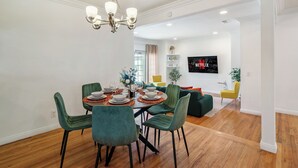 Un coin repas agrémenté d’un lustre, de chaises recouvertes d’un tissu vert et d’une table en bois dressée pour quatre personnes.