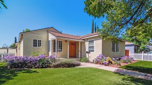 Une maison de plain-pied avec un porche à l’avant, une boîte aux lettres et une pelouse bien entretenue agrémentée de fleurs violettes.