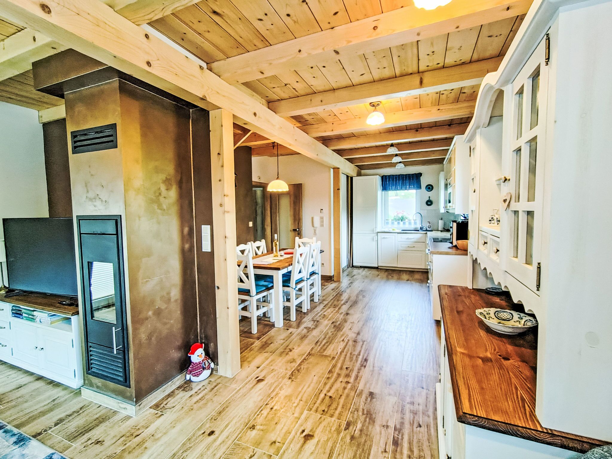 Una cocina amplia con vigas de madera, un comedor con sillas blancas y una chimenea acogedora.