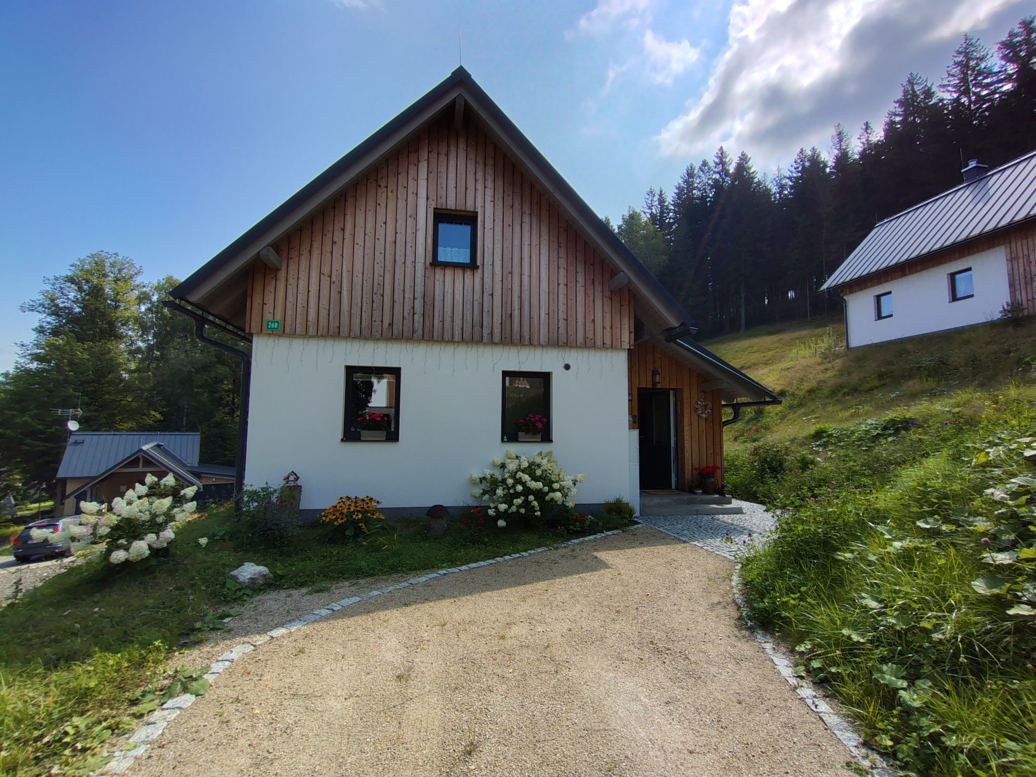 Une maison en bois avec un toit en pente, des murs blancs et une allée gravillonnée.