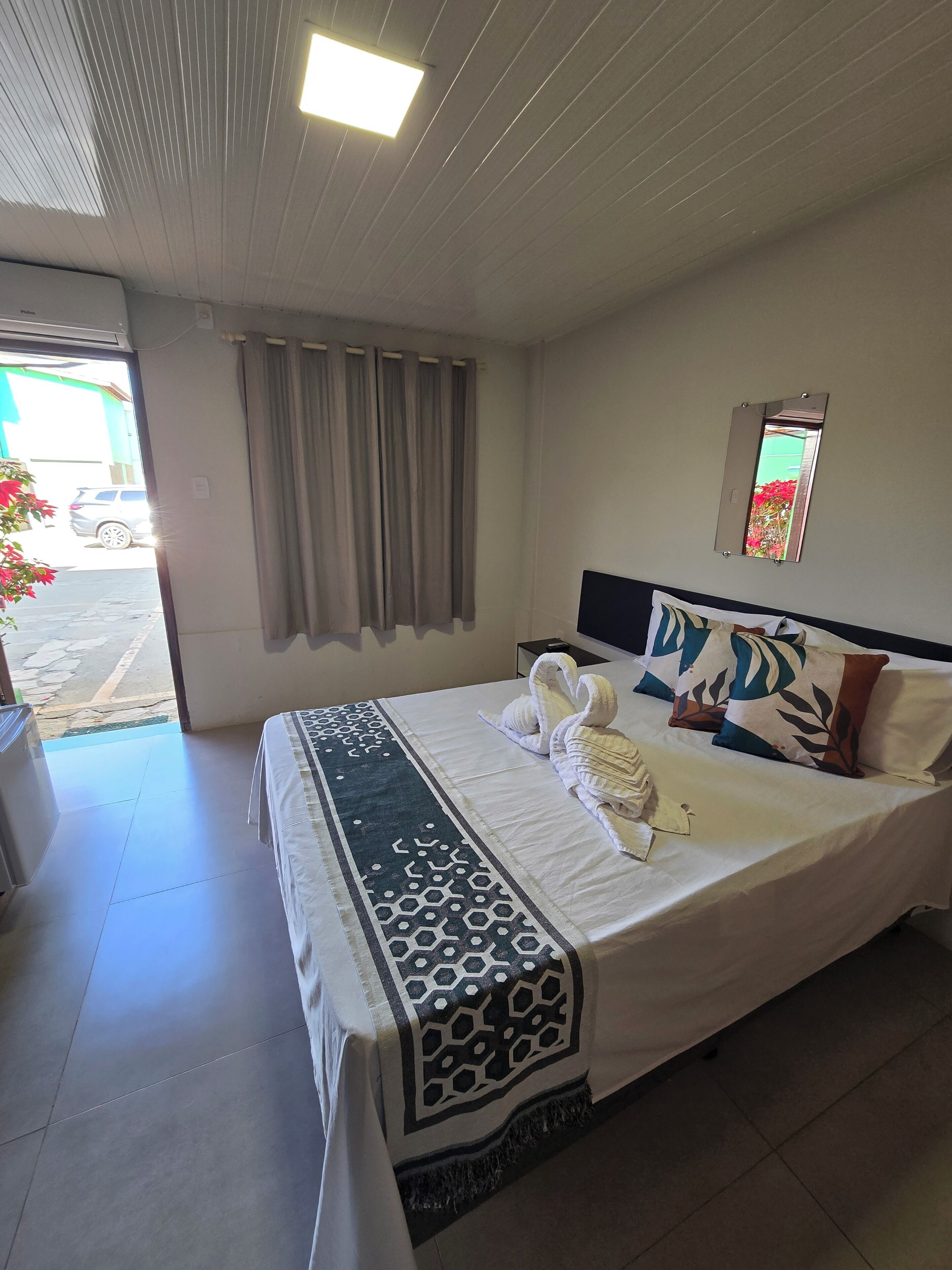 A hotel room with a bed, a mirror, and a view of the outside.
