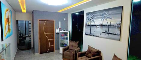 A modern living room with a marble floor, a refrigerator, a wooden door, and a painting of a tropical scene.