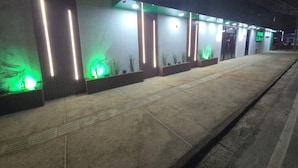 A nighttime view of a building with illuminated vertical light strips and planters with green lighting. - Pousada Elshaday (Vitória da Conquista)