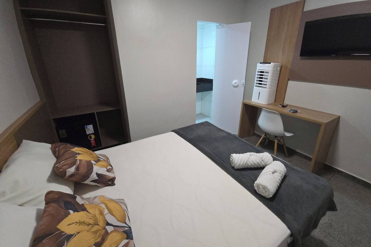 A hotel room with a bed, a desk, a chair, a TV, and a wardrobe.