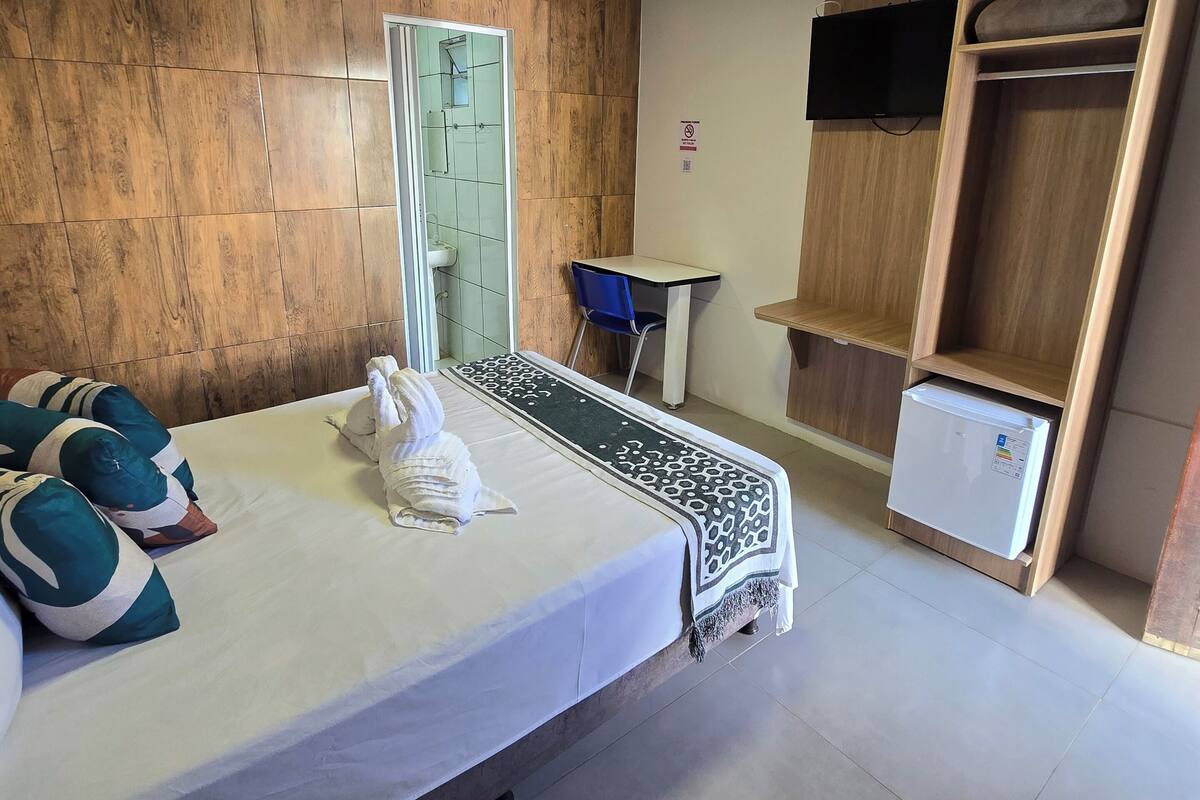 A hotel room with a bed, a small table, a TV, and a wardrobe.