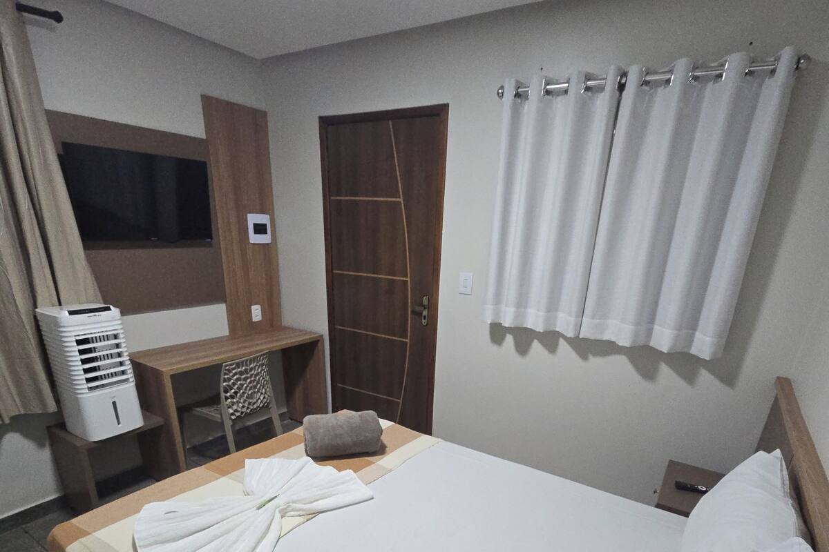 A hotel room with a bed, a desk, a chair, a TV, and a window.