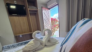 A hotel room with a bed, a TV mounted on the wall, a wooden wardrobe, and an air conditioning unit. - Pousada Elshaday (Vitória da Conquista)