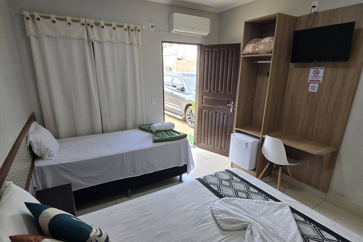 A hotel room with two beds, a TV mounted on a wooden cabinet, and a view of the street through an open door.