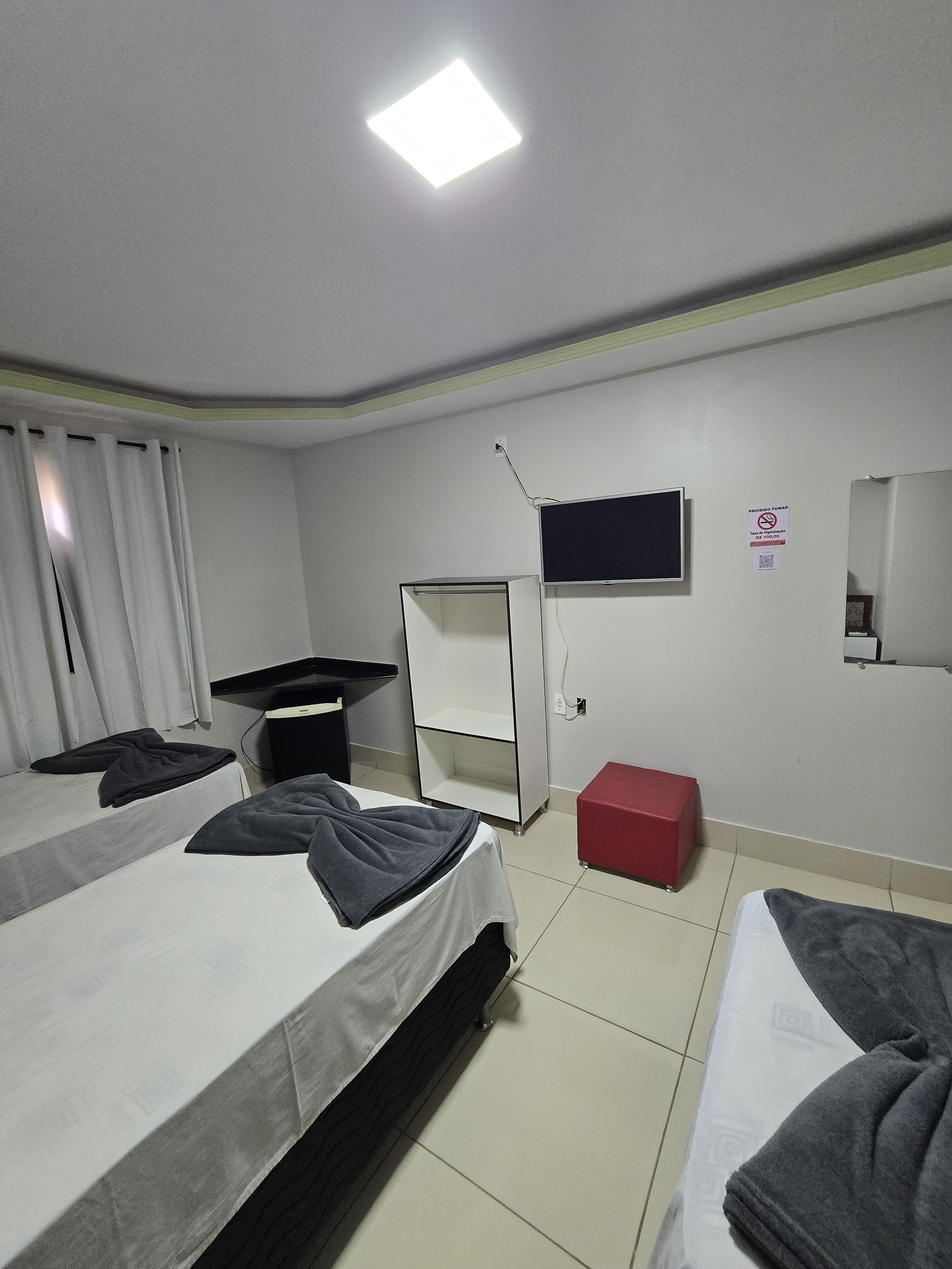 A hotel room with two beds, a desk, a TV, and a red box.