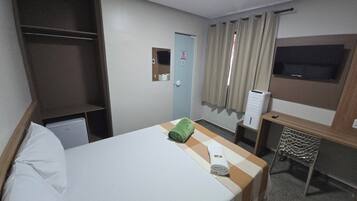 Quarto de hotel com cama, escrivaninha, televisão e guarda-roupa.