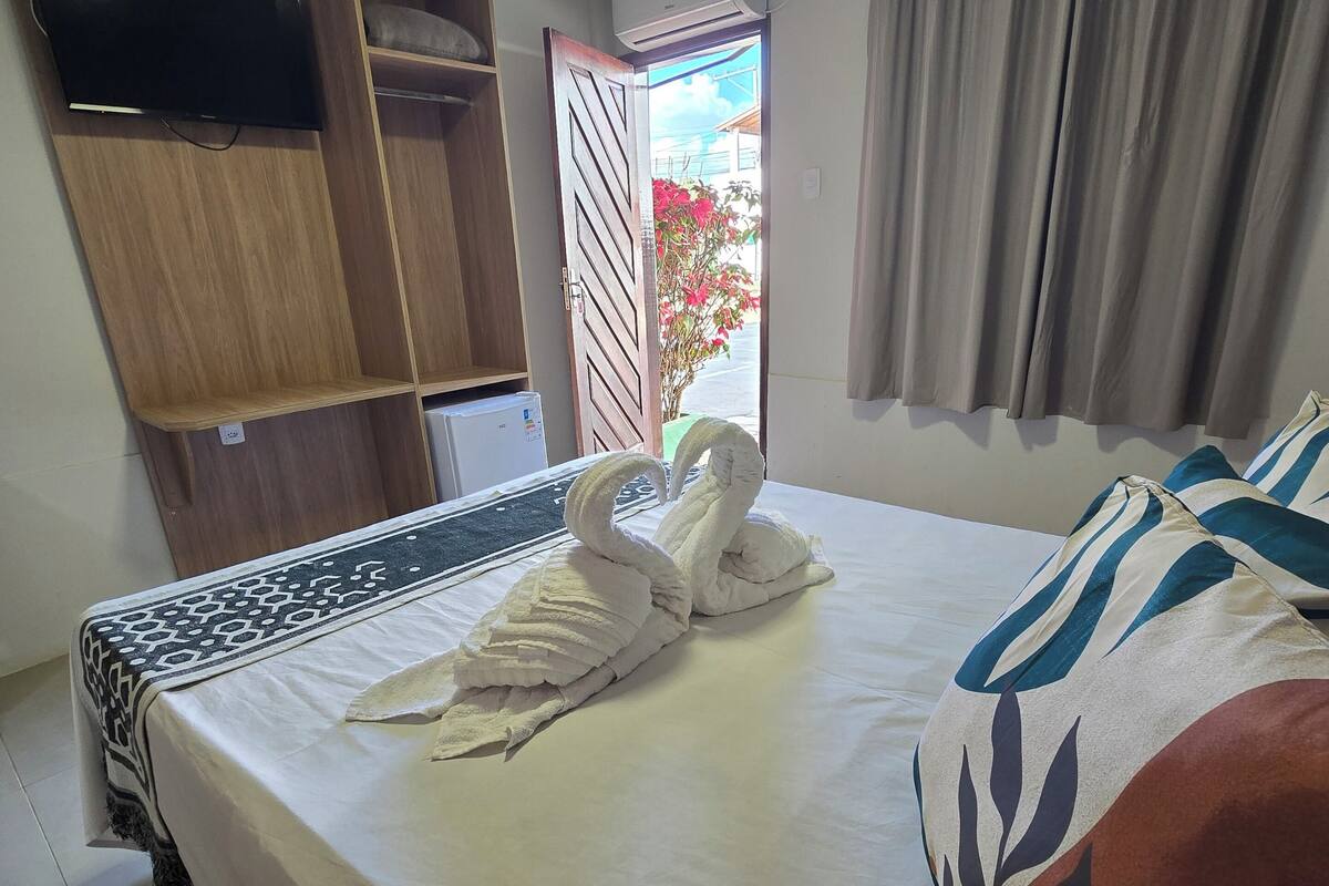 A hotel room with a bed, a wardrobe, a window with curtains, and a view of the outside.