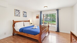 A bedroom with a wooden bed, a nightstand, and a window with curtains. - Brighton Retreat - Walk to Metro (Seattle)