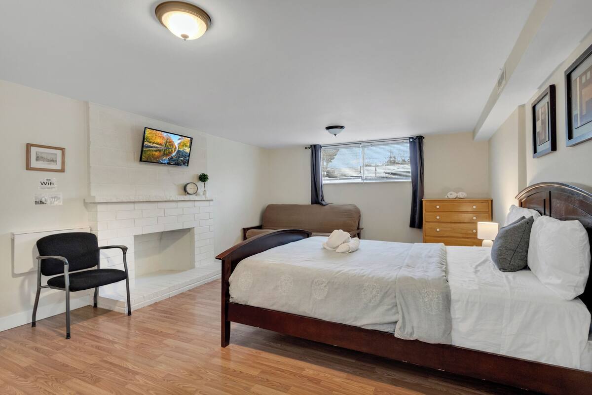A bedroom with a bed, a chair, a dresser, a TV, and a fireplace.