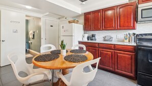 A modern kitchen with wooden cabinets, a black stove, and a dining area with a wooden table and white chairs. - Brighton Retreat - Walk to Metro (Seattle)