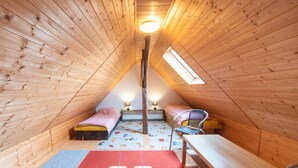 Un dormitorio estilo ático, pequeño y con paneles de madera, con dos camas, una mesa y una silla.