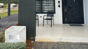 A modern building with a black door, a window with blinds, and a small outdoor seating area with two chairs. - Sunset Rose Retreat – 2BR Private Villa in Ocho Rios with 24-Hour Security (Ocho Rios)