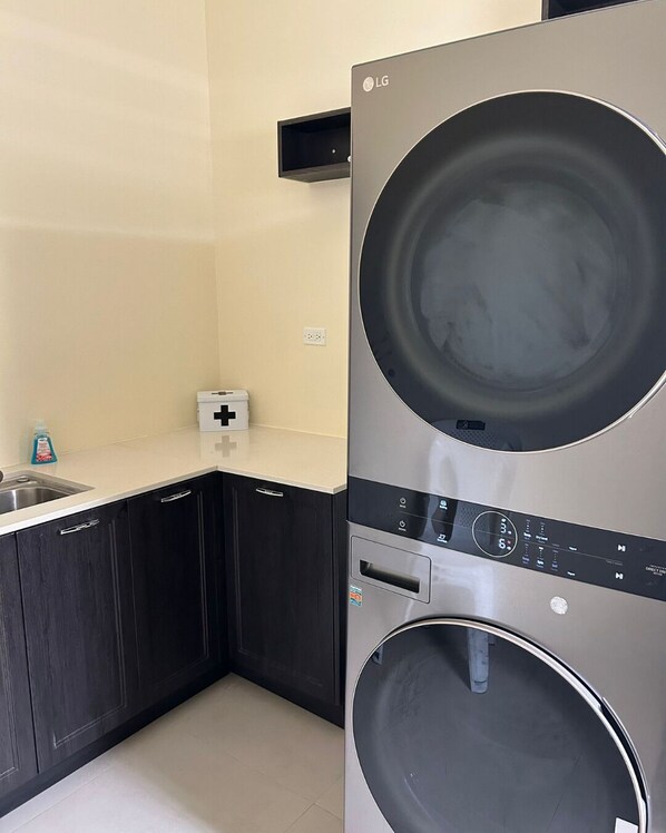 Une cuisine compacte avec des meubles de rangement sombres, un évier et un appareil combiné lave-linge et sèche-linge intégré.