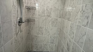 A shower with a handheld showerhead and a wall-mounted faucet, a metal shower tray, and a tiled wall with a marble-like pattern. - The Retro Carriage House (Denver)