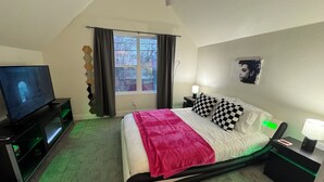 A bedroom with a bed, a TV, a window, and a nightstand. - The Retro Carriage House (Denver)