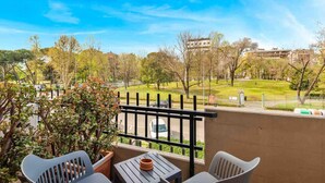 Een balkon met uitzicht op een park, een tafel en twee stoelen.