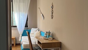 Een slaapkamer met een bed, nachtkastje, stoel, raam met dunne gordijnen en een wandlamp.