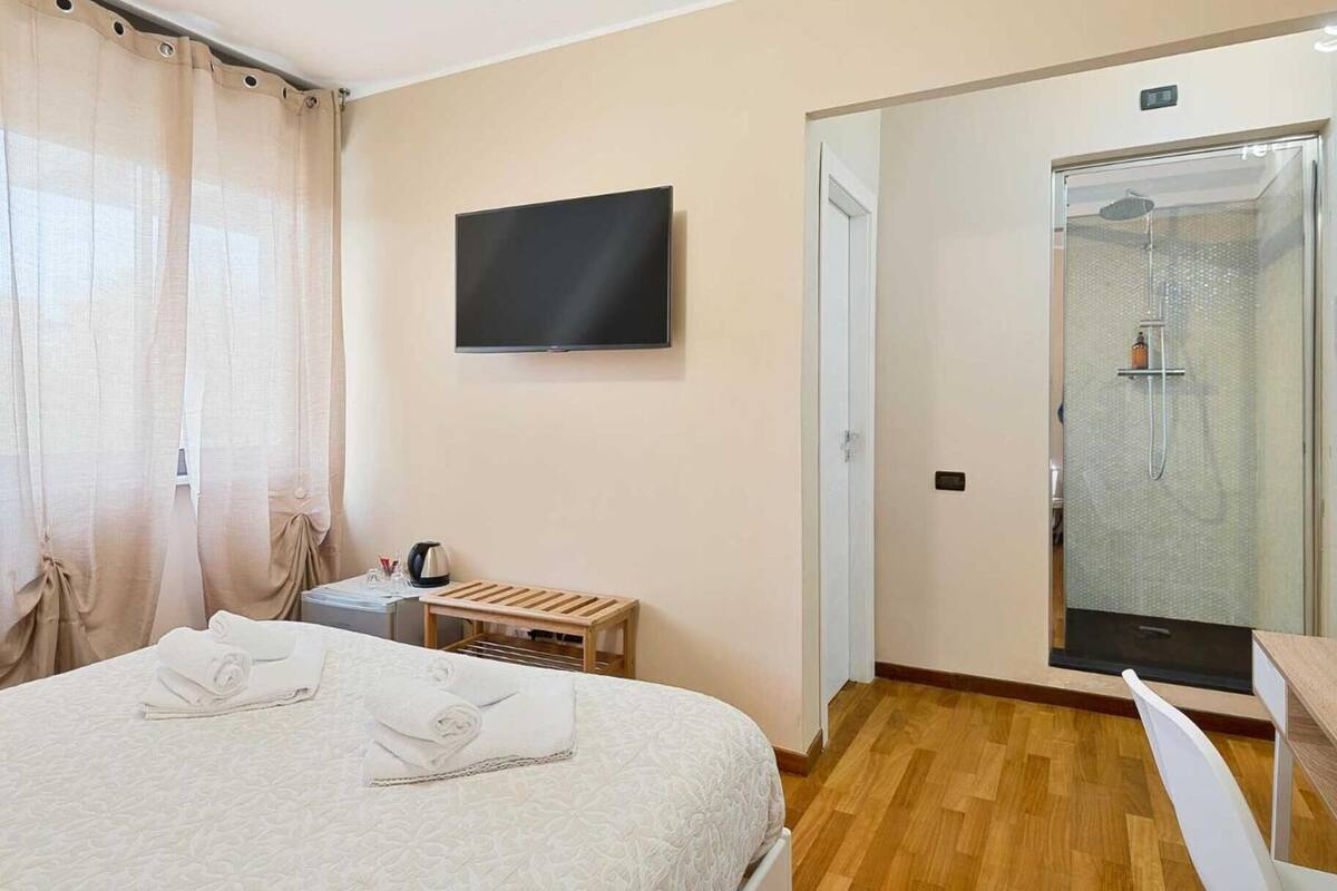Une chambre d’hôtel avec un lit, une télévision, une douche et une table de chevet en bois.