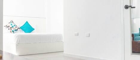 A modern bedroom with a bed, a TV mounted on the wall, and a door leading to another room.