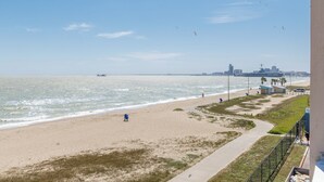 Une plage offrant une vue dégagée sur l’océan, un sentier longeant la côte et, au loin, le profil d’une ville.