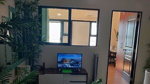 A living room with a television on a stand, a sofa, and several potted plants. - 1-bedroom condo with a magnificent Manila Bay sunset view. (Manila)