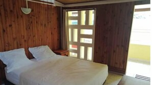 A bedroom with a large bed, wooden walls, a small bedside table, and a window with a view. - Entire 2-bedroom townhouse (Saint-Denis)