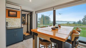 A modern kitchen with a large window, a dining table with chairs, and a view of the outdoors. - Modern PEI Shipping Container Retreat with Multiple Decks & Stunning Views (Oyster Bed Bridge)
