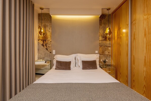 A modern hotel room with a large bed, two brown pillows, a glass side table, and a wooden wardrobe.