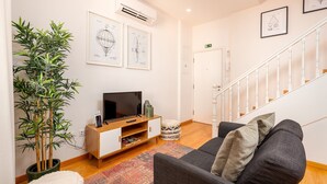 A modern living room with a flat-screen TV, a large potted plant, a grey sofa, and a staircase. - Charming Apartment in Oporto (Oporto)