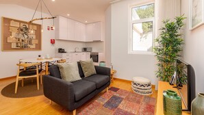A modern living room with a sofa, coffee table, and a dining area with chairs. There is a kitchen in the background with cabinets and appliances. - Charming Apartment in Oporto (Oporto)