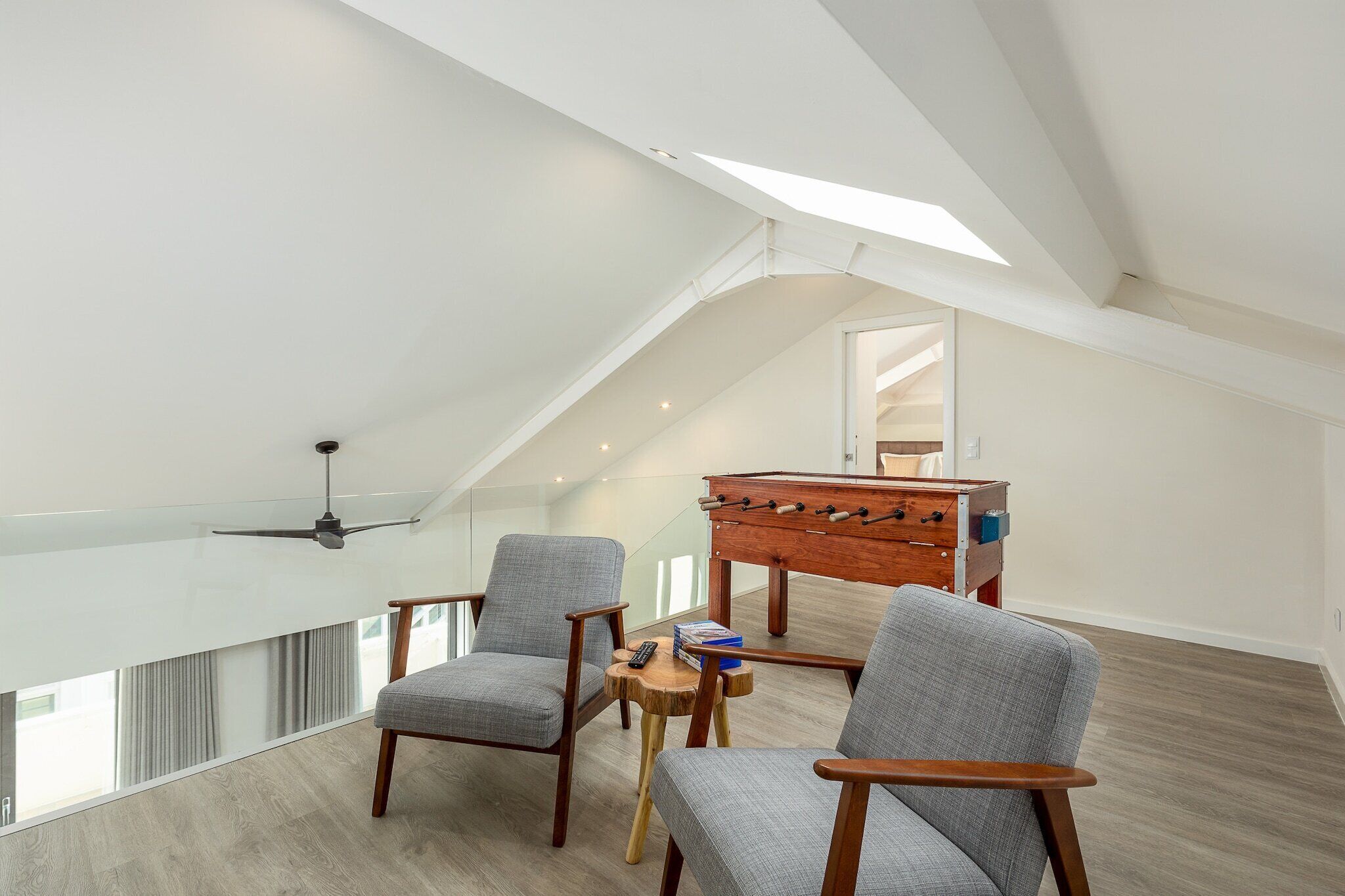 A spacious loft bedroom with a high ceiling, a ceiling fan, a wooden coffee table, and two grey armchairs.
