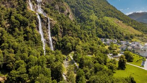 A mountainous landscape with a waterfall, lush greenery, and a small settlement with buildings.
