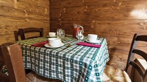 Un interior de madera con una mesa para dos, que incluye un mantel a cuadros, dos tazas blancas, una jarrón de vidrio y una cuchara.