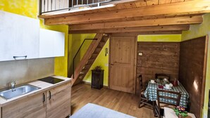 Cocina compacta con una escalera de madera, zona de comedor con mantel a cuadros y un pequeño rincón de estar.