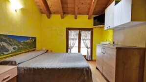 Una habitación con cama, vigas de madera en el techo, una zona de cocina y un cuadro en la pared.