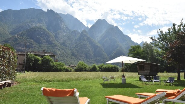 Zona verde con sillas de relax y una mesa bajo una sombrilla, con vistas a un paisaje montañoso.