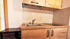 Una cocina compacta con microondas integrado, pileta de acero inoxidable y alacenas de madera.